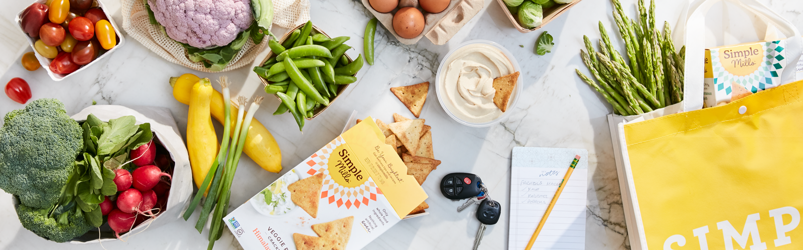 Simple Mills product boxes scattered across a tabletop along with yellow SImple Mills shopping bag