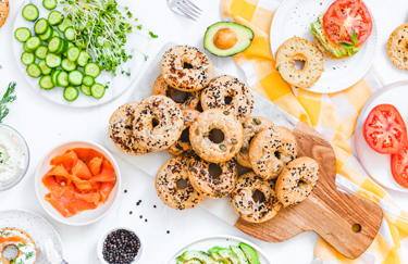 Assorted bagels sorrounded by toppings including fresh cut vegetables salmon and cream cheese