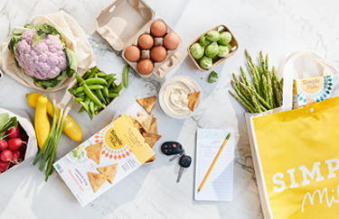 Woman holding a basket fillet with groceries including Simple Mills Almond Flour Baking Mixes