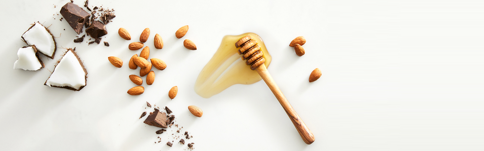 Raw coconut pieces, scattered almonds and honey spread across white marble countertop