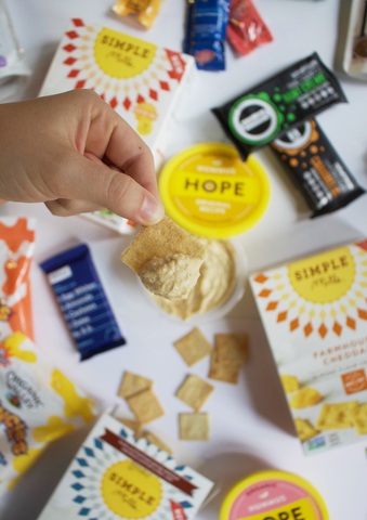 Hand scooping hummus with Simple Mills Farmhouse Cheddar Almond Flour Cracker