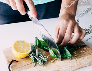 Woman's hand chopping fresh herbs on cutting board with fresh lemon