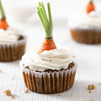 Cupcake with vanilla icing topped with a fresh carrot top msde using both Simple Mills cupcake mix and vanilla frosting