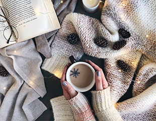 hygge-1.jpg Various sweater and cozy materials, person cradling cup of hot beverage