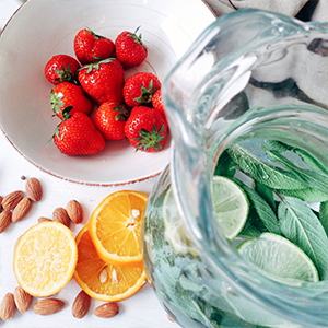 Pitcher of water with various herbs and limes with strawberries cut oranges and almonds