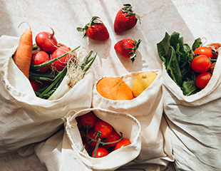 Four white burlap bags filled with fresh colorful vegetables