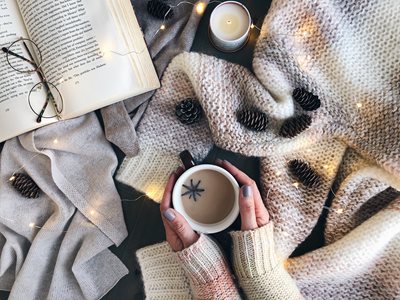 overhead-shot-of-cozy-winter-sweater-scarf-book-candle-pine-cones-fairy-lights-and-woman-s-hands-a_t20_6lp3ov-(1).jpg