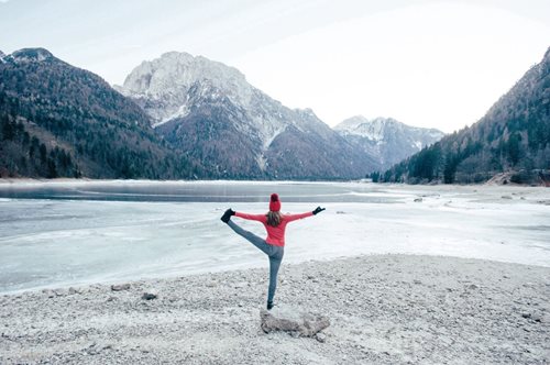 Person in balancing yoga pose in front of mountains and frozen lake